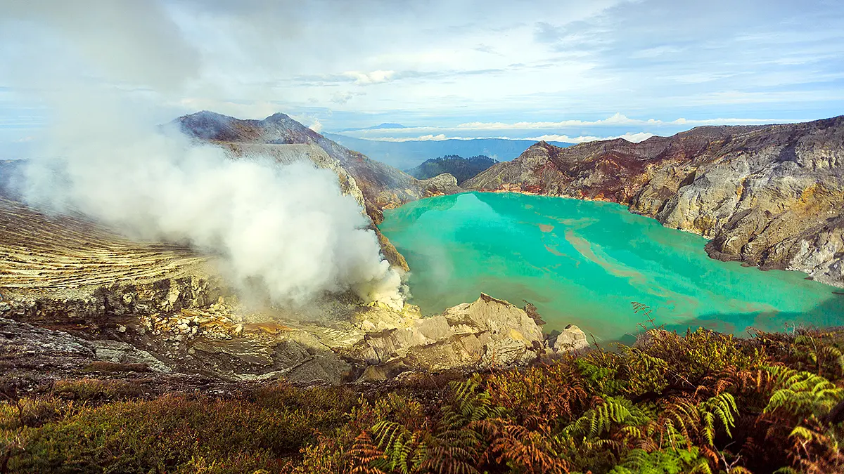 Turquoise acidic crater lake of Kawah Ijen with dense volcanic steam rising from fumaroles along the crater wall