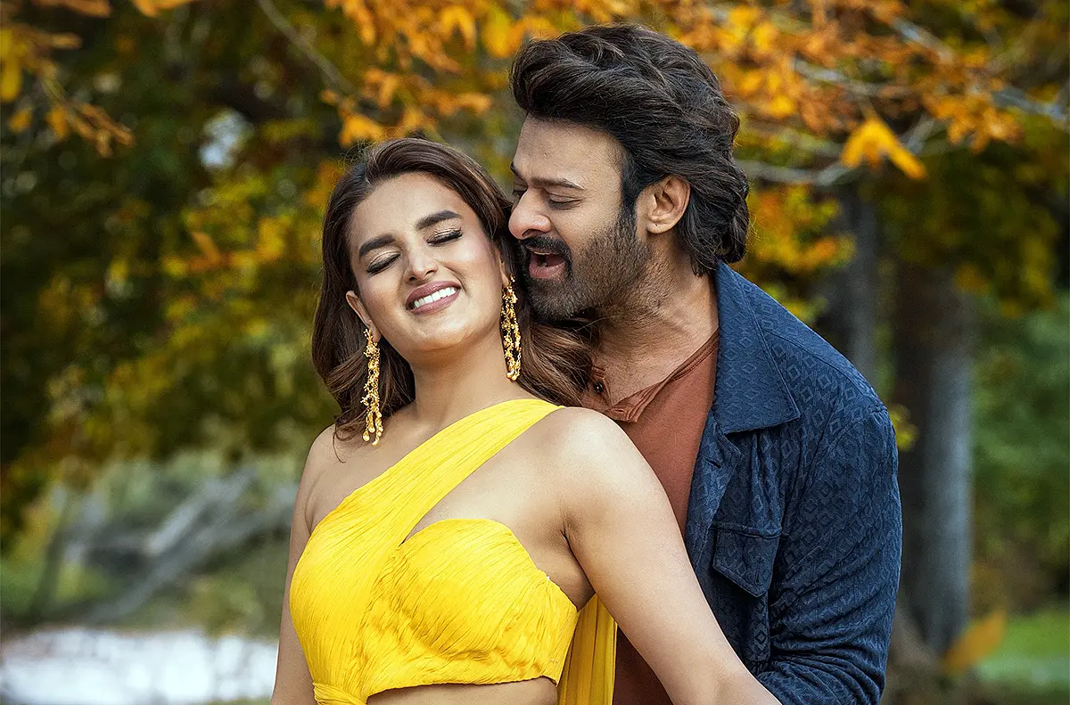 Prabhas and Nidhhi Agerwal in a romantic song sequence from The Raja Saab with bright outdoor visuals.