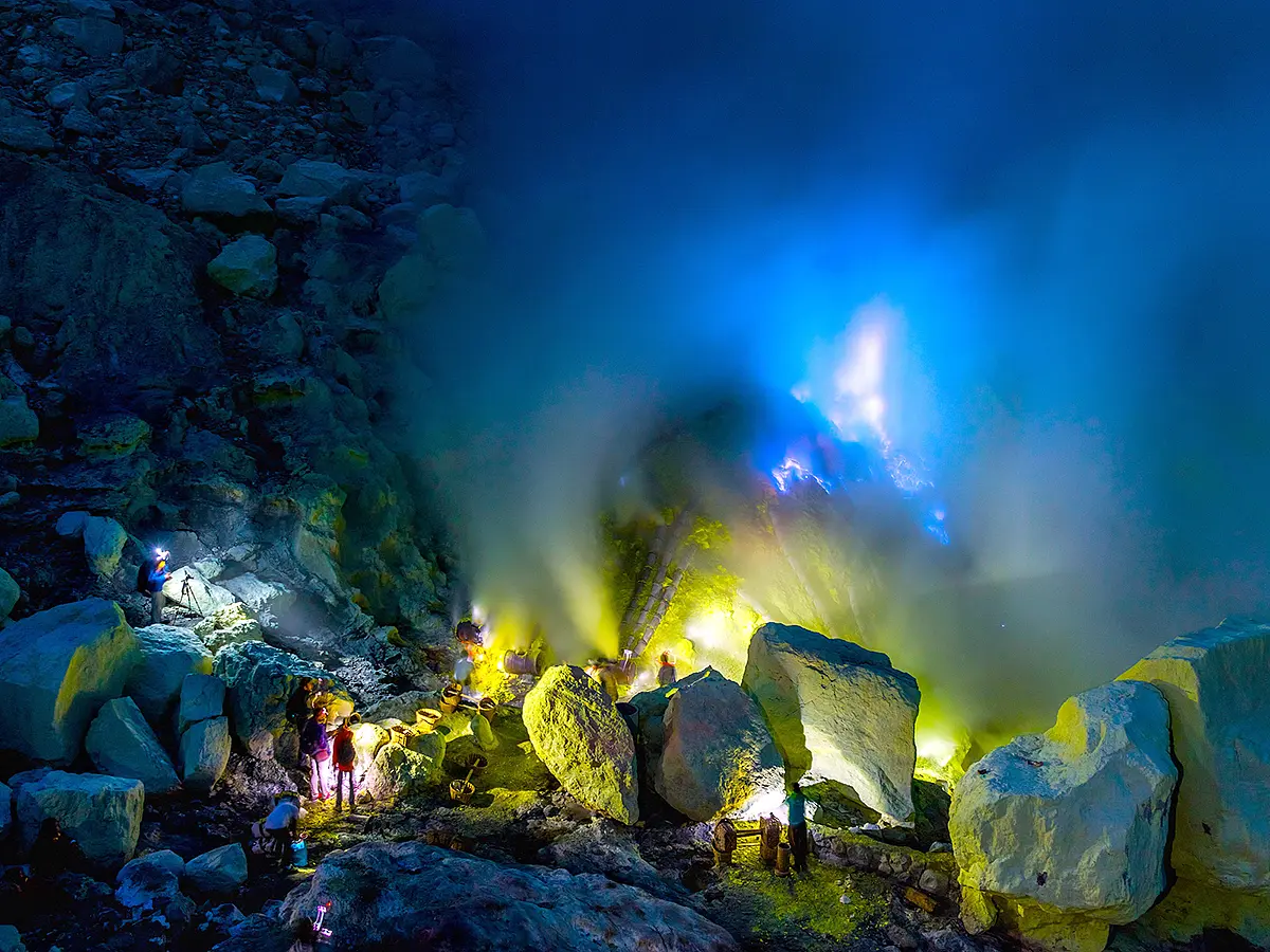 Sulphur miners working at night near blue flames and thick volcanic smoke inside Kawah Ijen crater