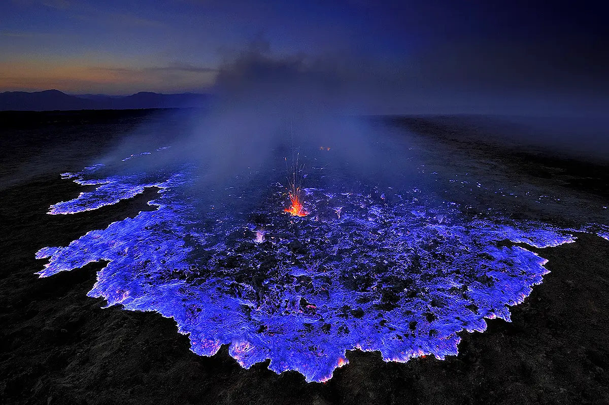 Bright blue lava flowing over volcanic ground at Kawah Ijen crater in Indonesia, caused by burning sulfur gases at night