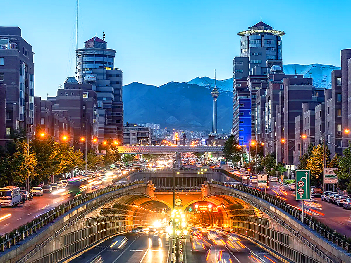 Beautiful Tehran cityscape featuring Milad Tower, glowing traffic lights, and Alborz mountains in the backdrop during evening