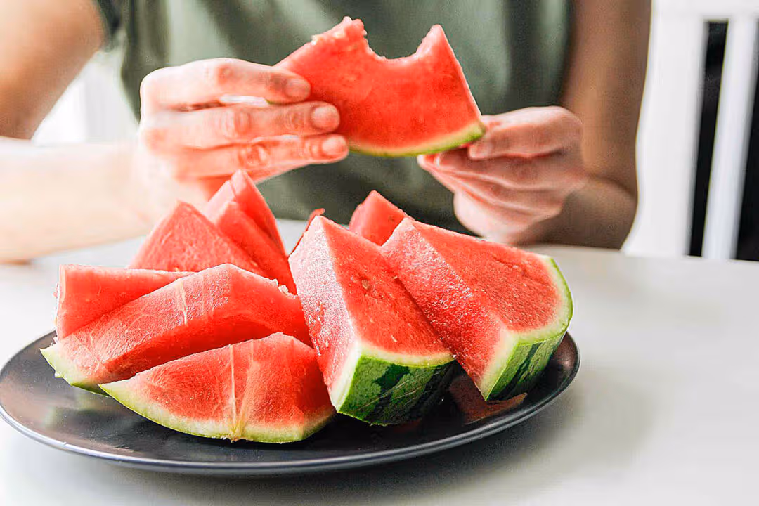 Person eating fresh watermelon slices at dining table healthy summer fruit concept