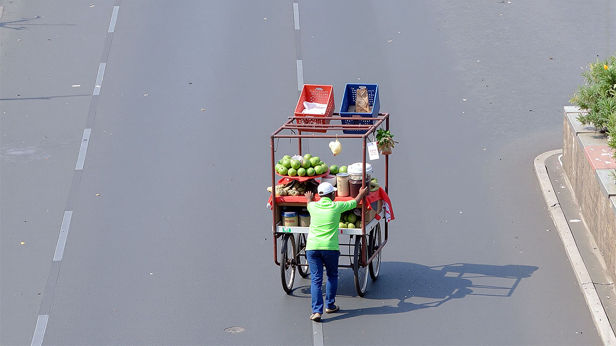 Street vendor pushing cart on empty road during intense summer heat